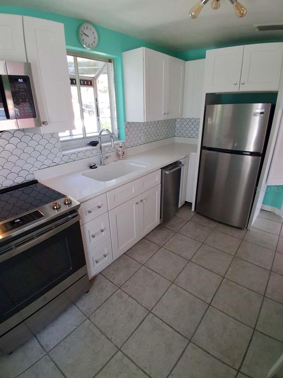 A kitchen features white cabinets, stainless steel appliances, a tiled backsplash, and light-colored floor tiles — 3372 MAYFLOWER STREET, SARASOTA, FL