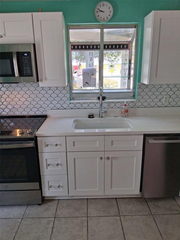 A kitchen features white cabinets, a stainless steel stove, a sink, and scalloped tile backsplash — 3372 MAYFLOWER STREET, SARASOTA, FL