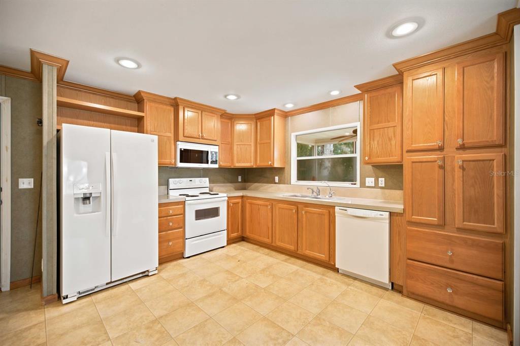 A kitchen with wood cabinets, white appliances, tile flooring, and a window above the sink — 22925 SW 117TH STREET, DUNNELLON, FL