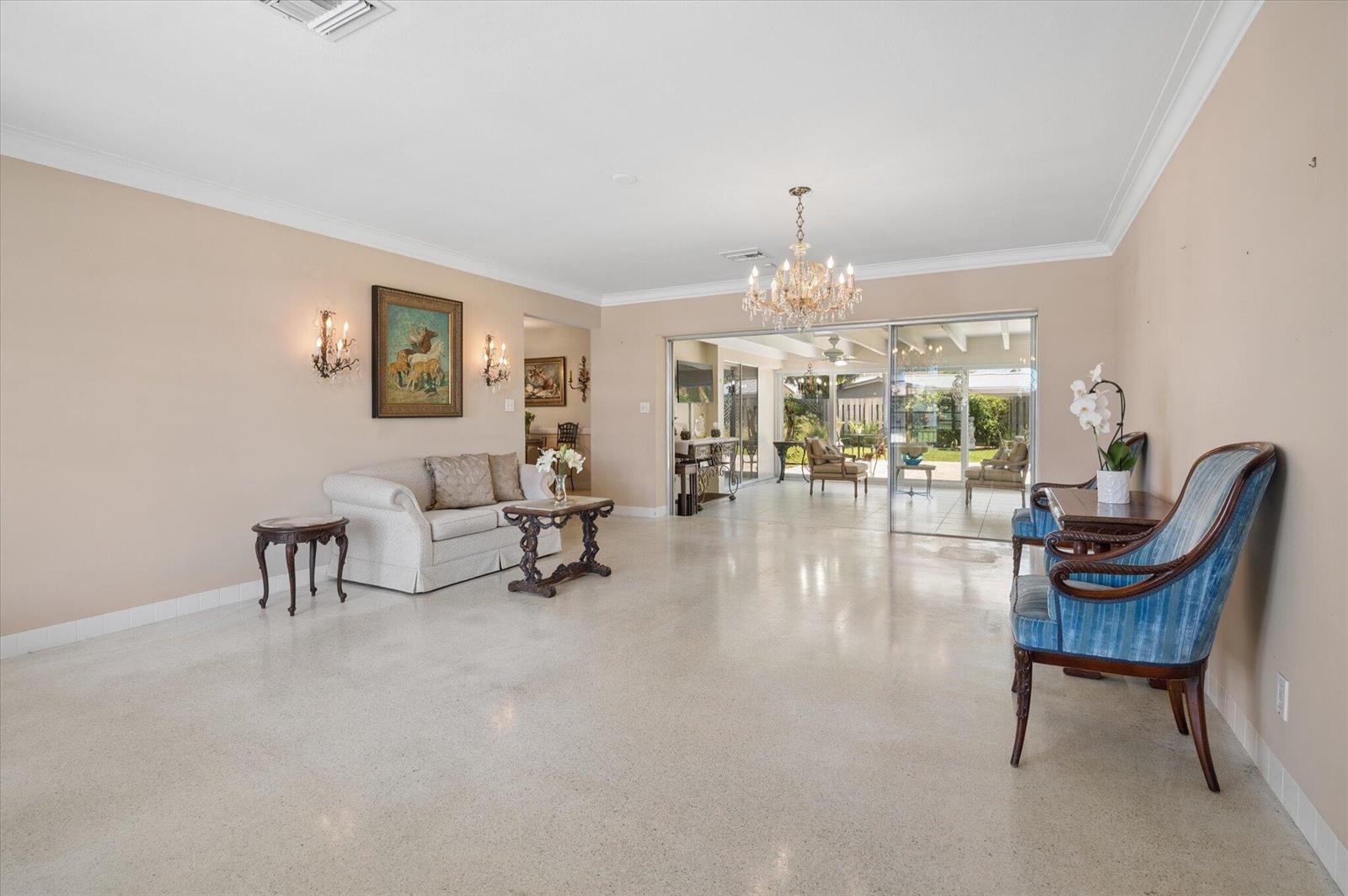A spacious living room features light-colored terrazzo flooring, a crystal chandelier, and sliding glass doors — 611 SE 11th Street, Pompano Beach FL 33060, POMPANO BEACH, FL