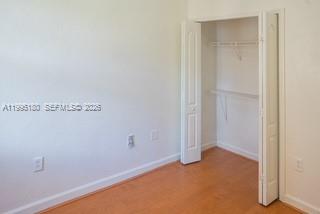 A bedroom with light-colored walls, wood-look flooring, and an open white closet — 7070 NW 177th St # 10, Hialeah FL 33015, HIALEAH, FL