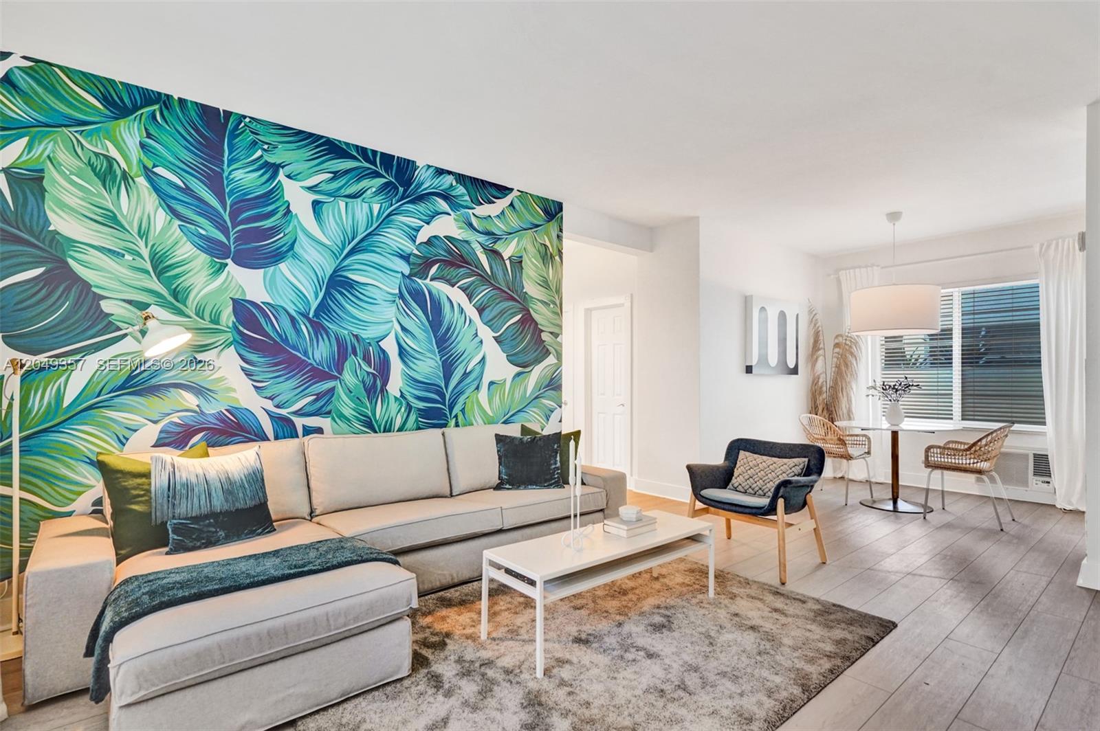 A living room features a large tropical leaf mural, a sectional sofa, and dining area — 1431 Lincoln Ter # 1, Miami Beach FL 33139, MIAMI BEACH, FL