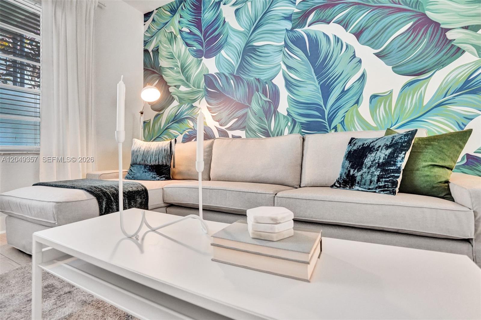 A living room features a sectional sofa against a wall with large tropical leaf wallpaper — 1431 Lincoln Ter # 1, Miami Beach FL 33139, MIAMI BEACH, FL