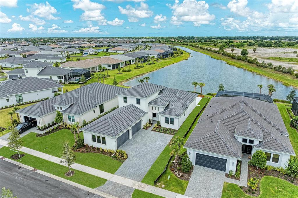 An aerial view shows several modern suburban houses with gray tiled roofs near a lake — 4517 MONDRIAN COURT, SARASOTA, FL