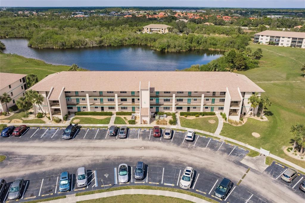 An aerial view shows a multi-story apartment building with a parking lot and a lake — 175 KINGS HIGHWAY UNIT 538, PUNTA GORDA, FL