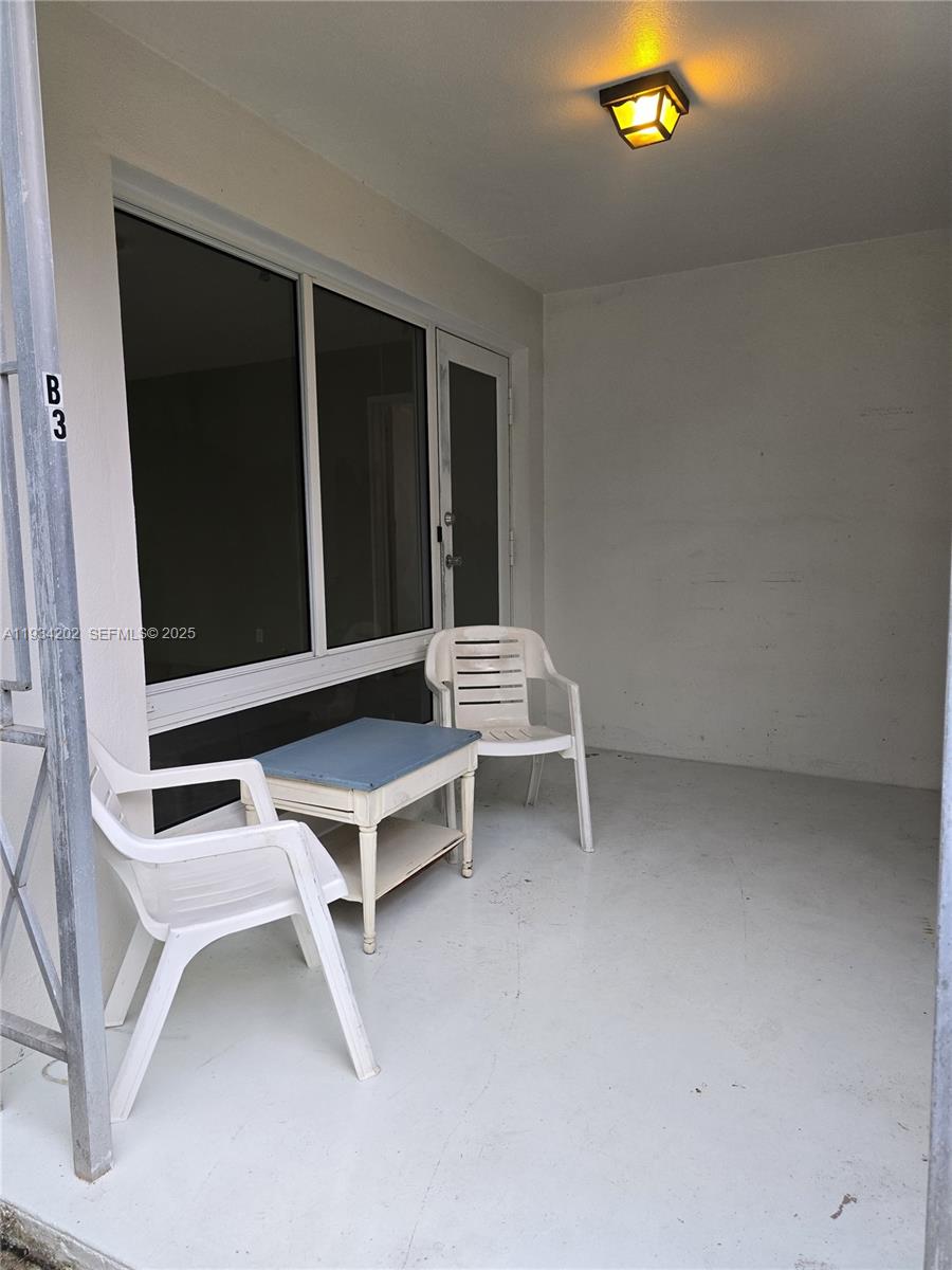 A covered patio features a white floor, two plastic chairs, a small table, and a light — 3201 SE 12th St # B3, Pompano Beach FL 33062, POMPANO BEACH, FL