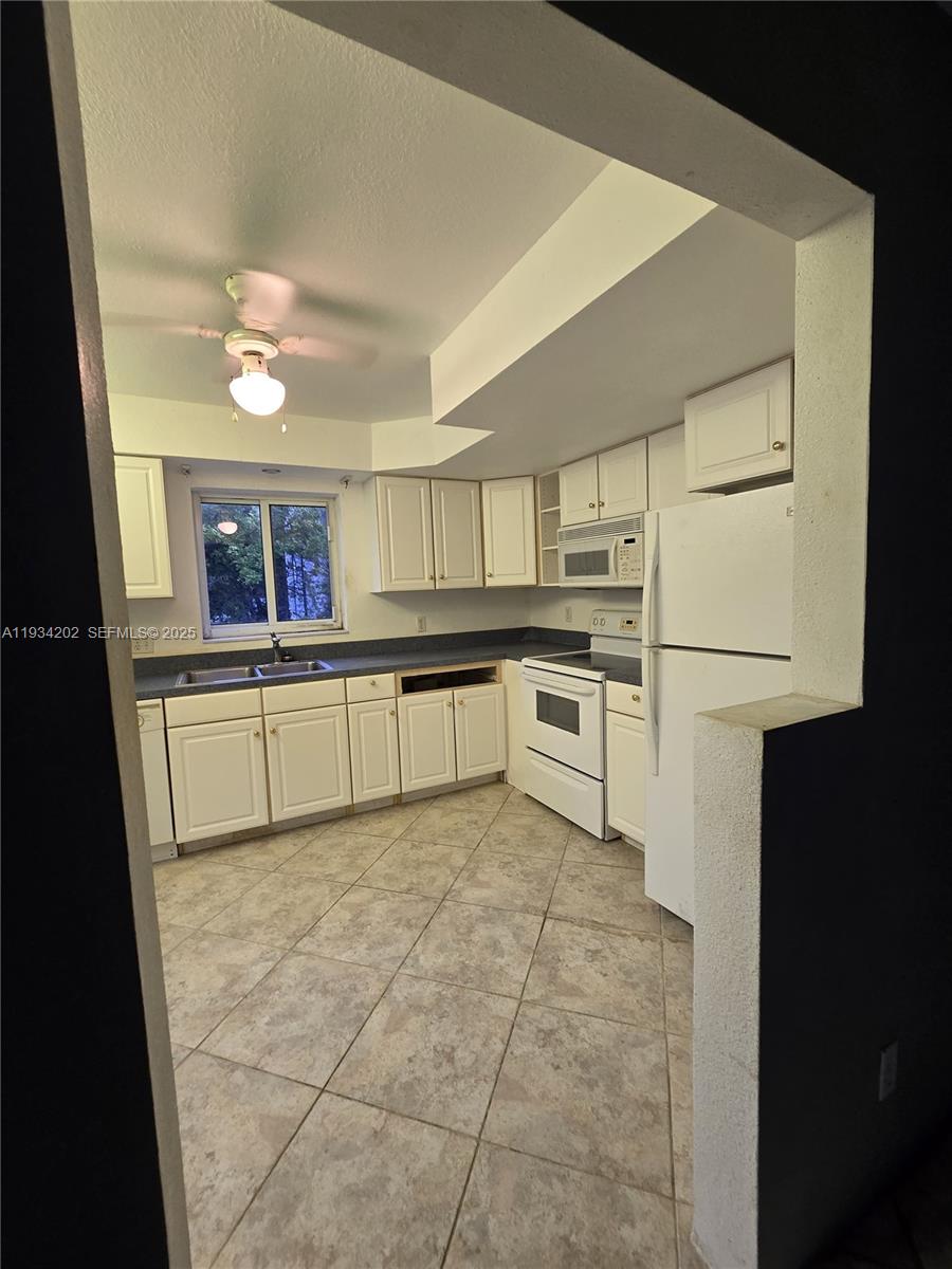 A kitchen features white cabinets, white appliances, a double sink, and light-colored tile flooring — 3201 SE 12th St # B3, Pompano Beach FL 33062, POMPANO BEACH, FL