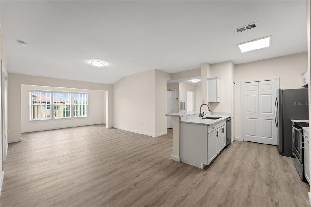 An open-concept living area with light wood-look flooring, a kitchen island, and large windows — 5447 VINELAND ROAD UNIT 1308, ORLANDO, FL