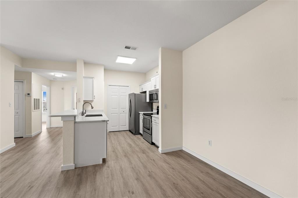 A kitchen with white cabinets, stainless steel appliances, and light wood-look flooring — 5447 VINELAND ROAD UNIT 1308, ORLANDO, FL