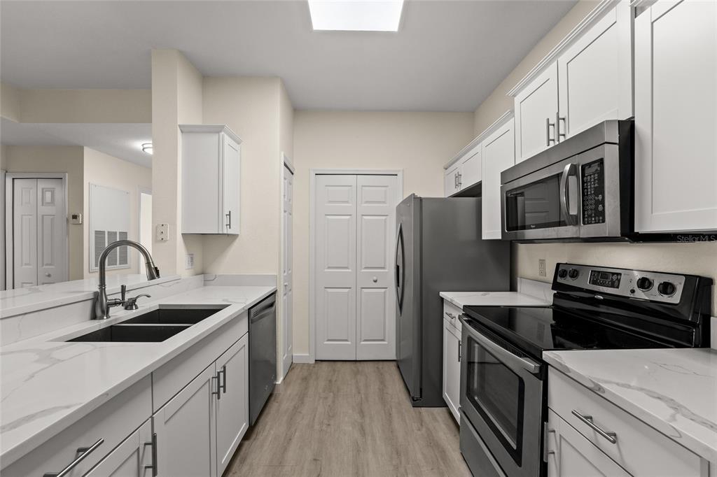 A galley kitchen features white cabinets, marble-look countertops, stainless steel appliances, and light wood flooring — 5447 VINELAND ROAD UNIT 1308, ORLANDO, FL