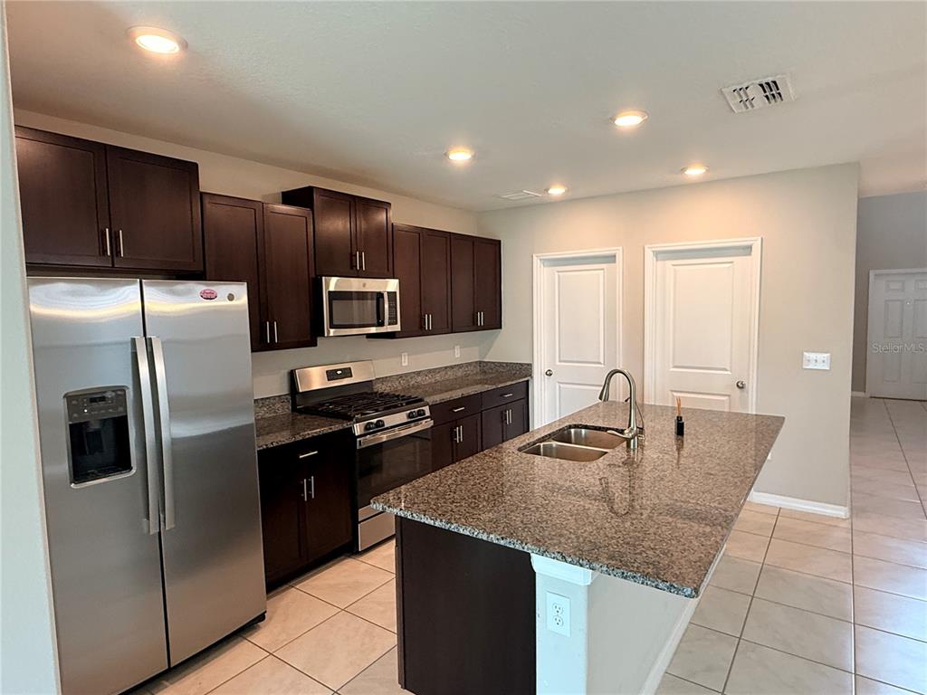 A kitchen features dark wood cabinets, granite countertops, stainless steel appliances, and a central island — 10363 SHADY PRESERVE DRIVE, RIVERVIEW, FL