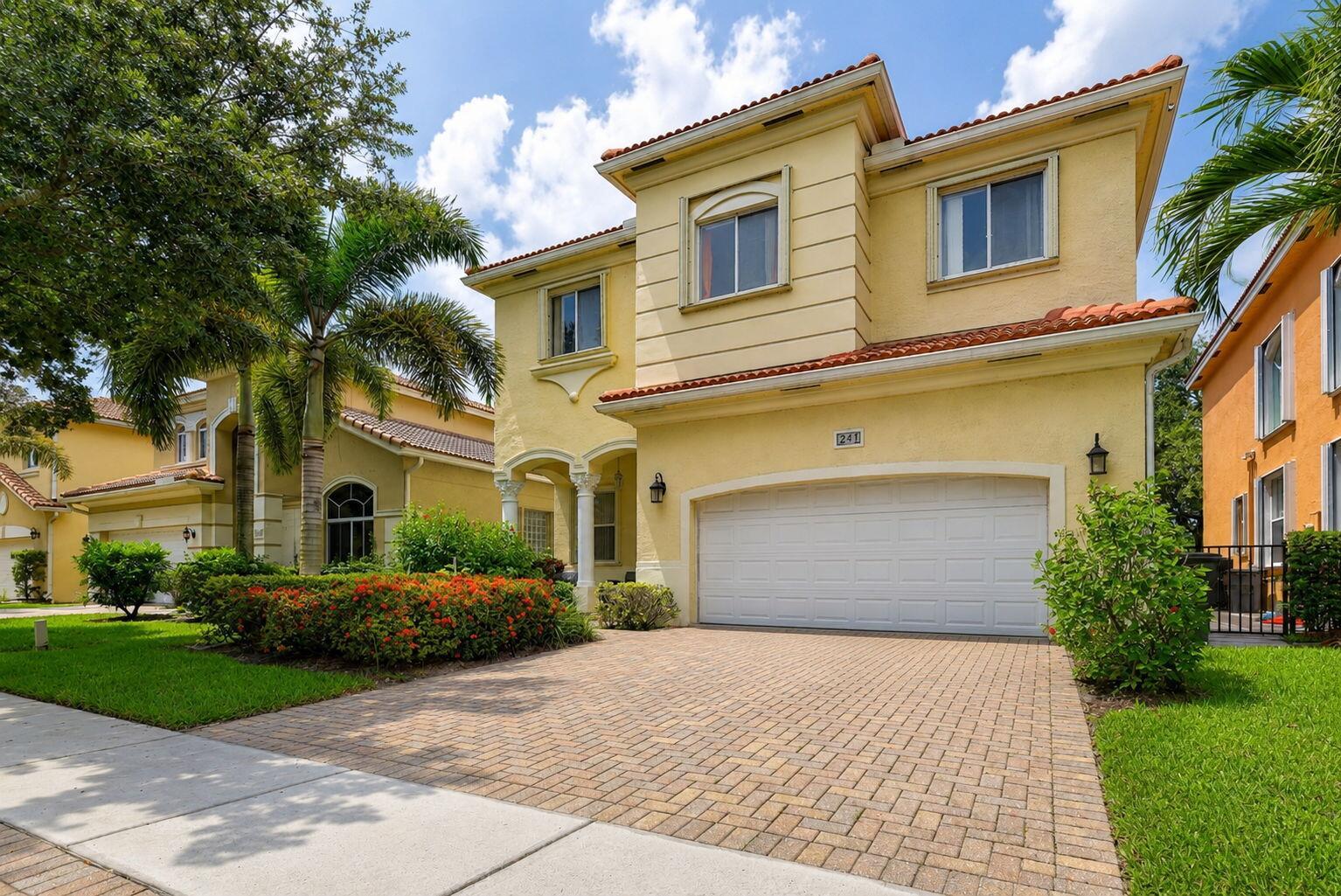 A two-story yellow stucco house with a tiled roof, paved driveway, and palm trees — 241 Gazetta Way, West Palm Beach FL 33413, WEST PALM BEACH, FL