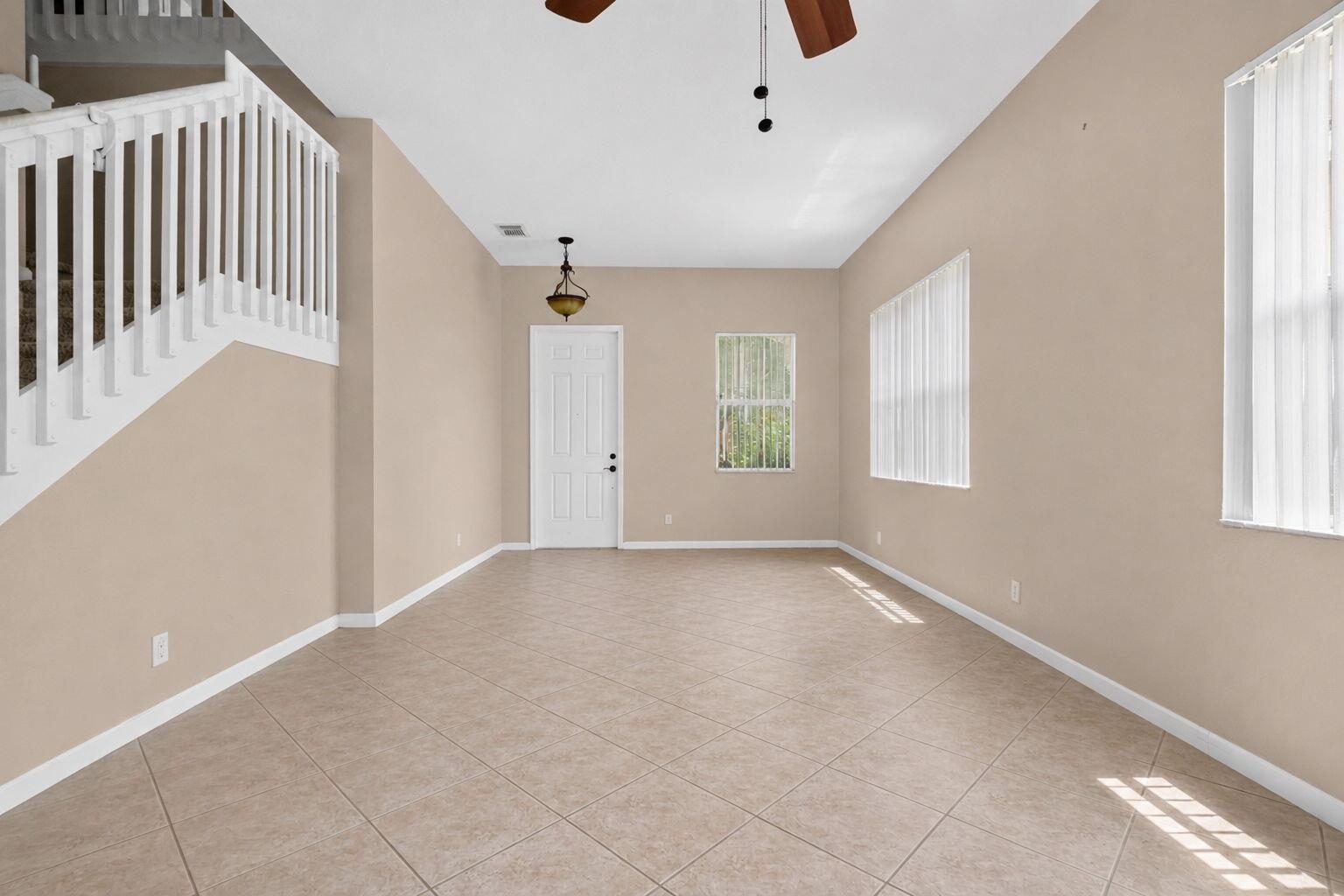 An empty room with beige walls, tile flooring, a white staircase, and two windows — 241 Gazetta Way, West Palm Beach FL 33413, WEST PALM BEACH, FL