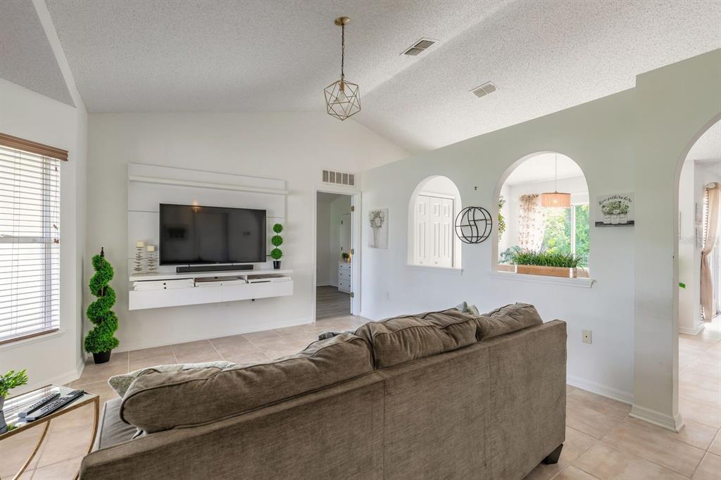 A living room features a wall-mounted television, a brown sofa, and arched wall cutouts — 18 LEE DRIVE, PALM COAST, FL