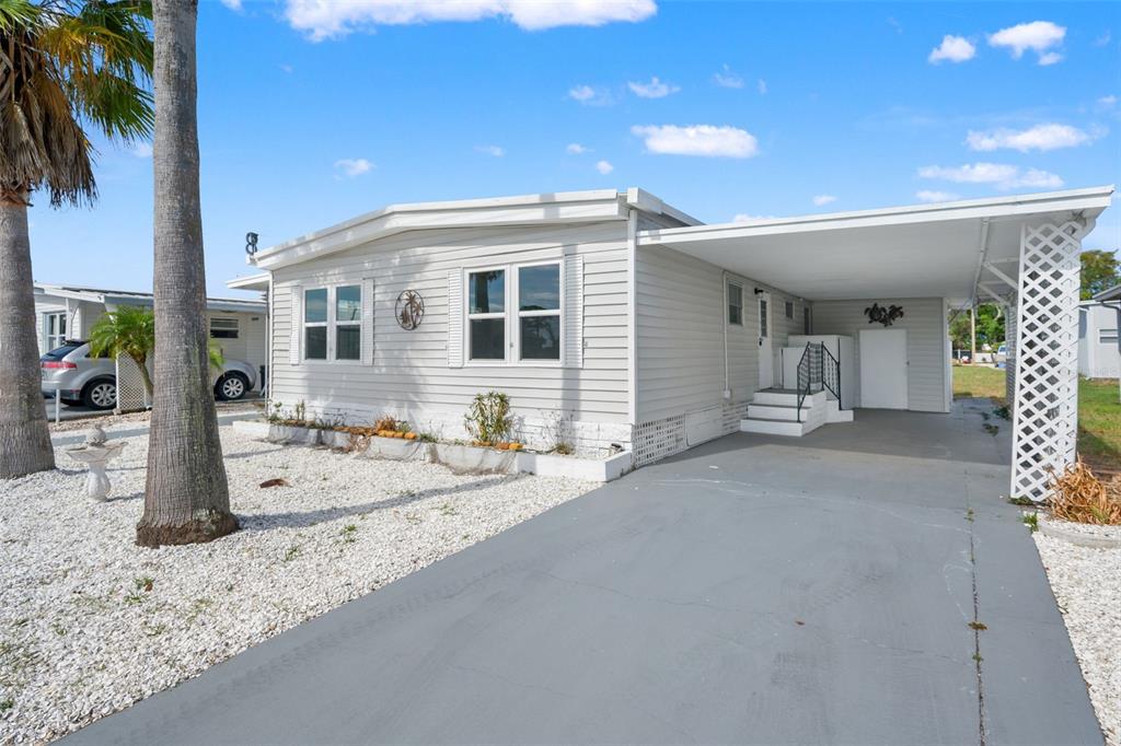 A light gray mobile home with a carport, white lattice trim, and a gravel front yard — 12019 CARTWRIGHT DRIVE, HUDSON, FL