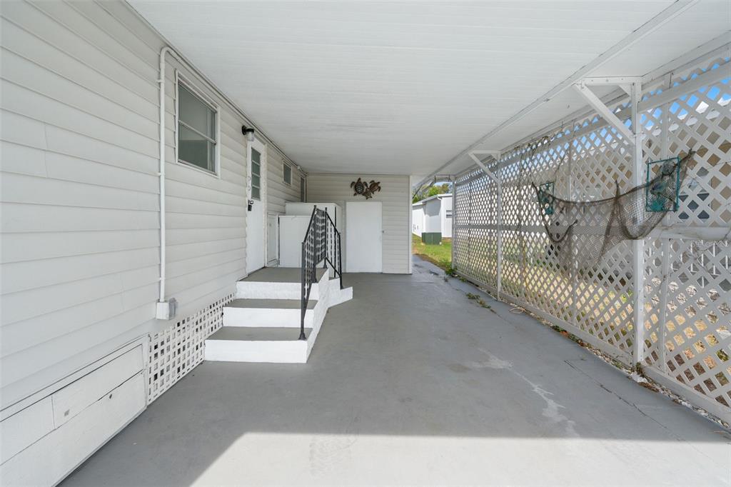 A covered carport features white siding, concrete flooring, stairs with a railing, and lattice screening — 12019 CARTWRIGHT DRIVE, HUDSON, FL