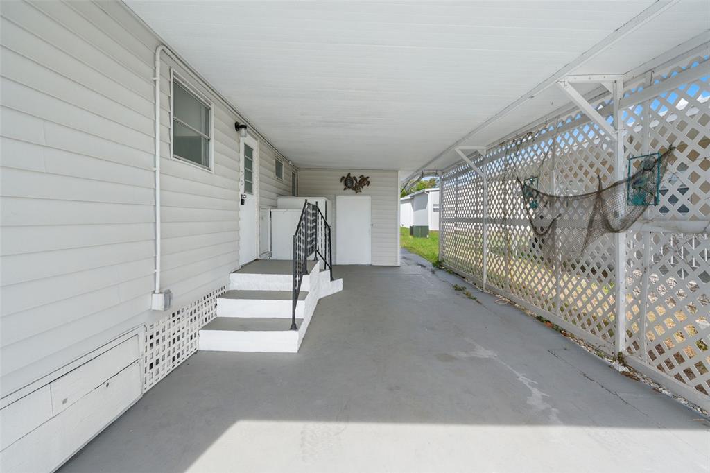 A covered carport with white siding, concrete flooring, and a white lattice privacy screen — 12019 CARTWRIGHT DRIVE, HUDSON, FL