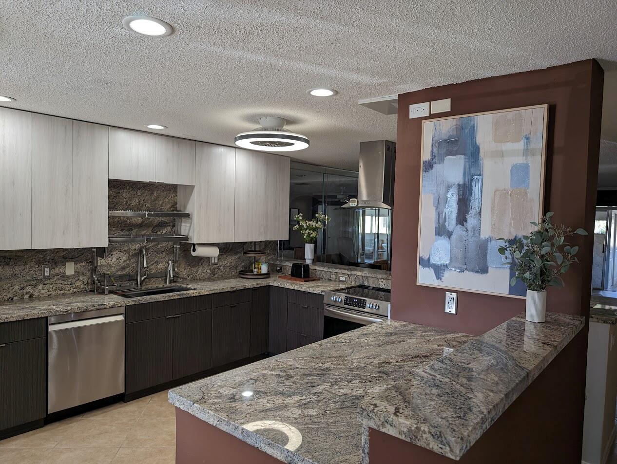 A modern kitchen features two-toned cabinetry, granite countertops, stainless steel appliances, and a brown accent wall — 1710 NW 18th Avenue # 204, Delray Beach FL 33445, DELRAY BEACH, FL