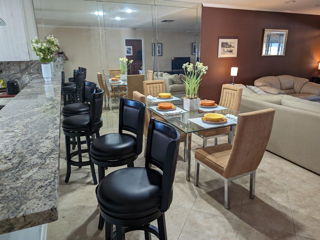 A dining area with a glass table and tan chairs sits beside a granite breakfast bar — 1710 NW 18th Avenue # 204, Delray Beach FL 33445, DELRAY BEACH, FL
