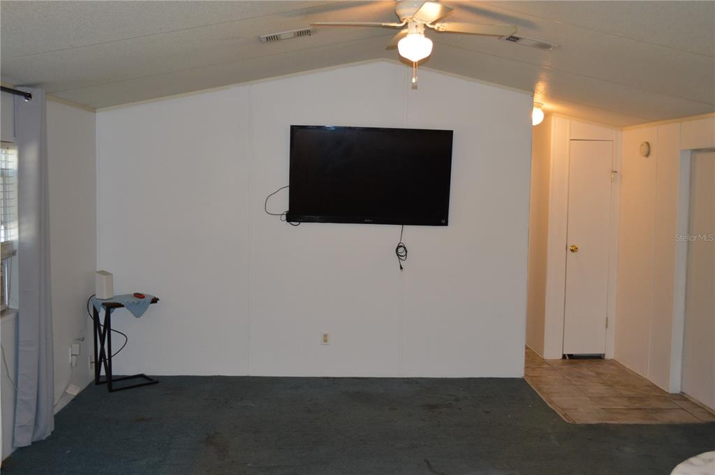 A living room features a wall-mounted television, a ceiling fan, and blue carpeting — 349 ELAND DRIVE, NORTH FORT MYERS, FL