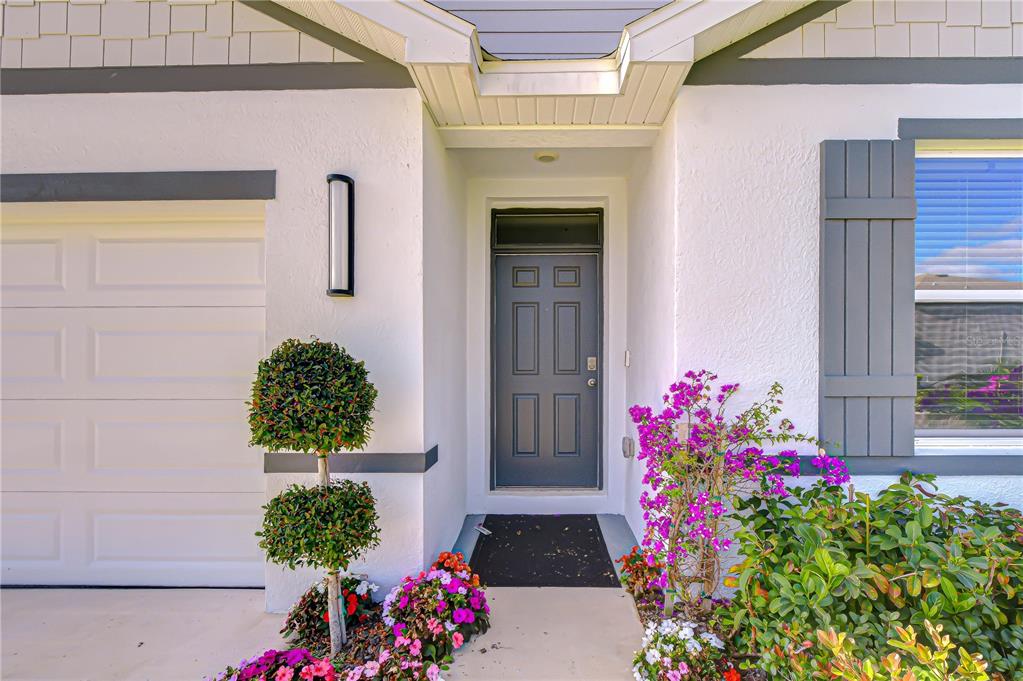 A front entrance features a gray door, a garage, and landscaping with pink flowers — 2763 WIDEWATER WAY, ZEPHYRHILLS, FL