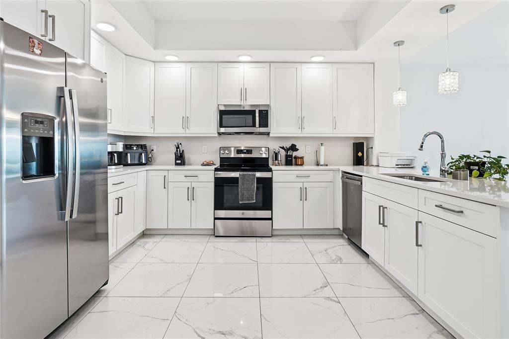 A modern kitchen features white cabinetry, stainless steel appliances, and white marble-patterned tile flooring — 415 ISLAND WAY UNIT 204, CLEARWATER, FL