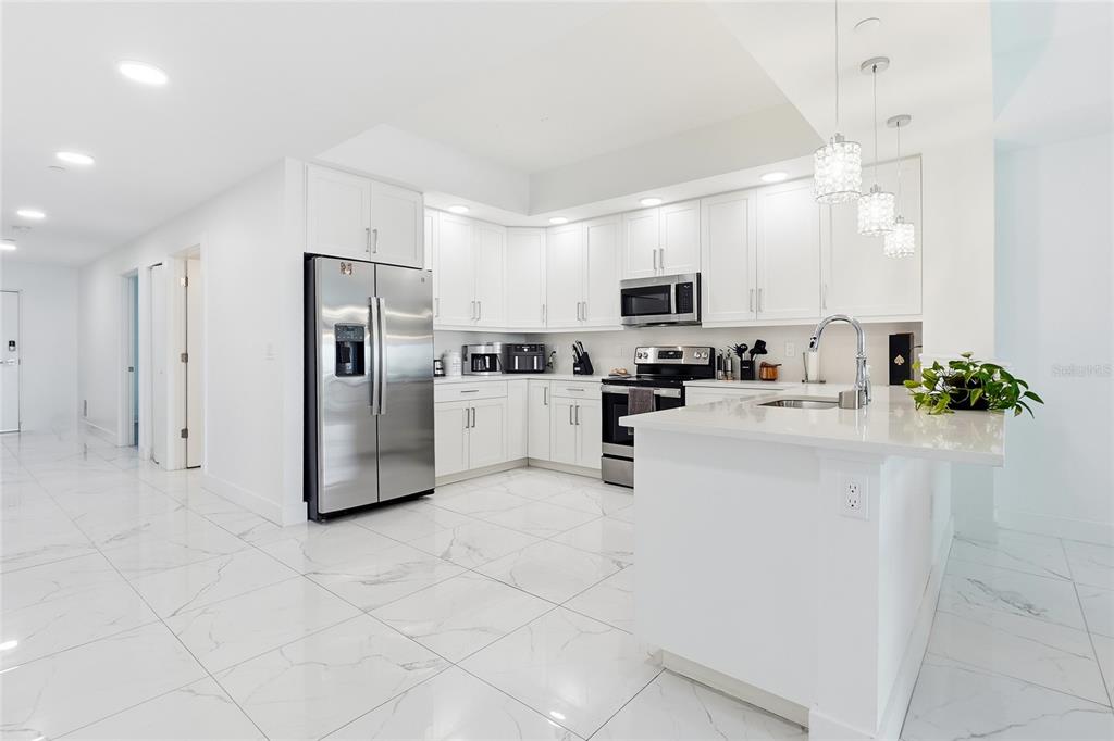 A modern kitchen features white cabinetry, stainless steel appliances, and white marble-patterned tile flooring — 415 ISLAND WAY UNIT 204, CLEARWATER, FL