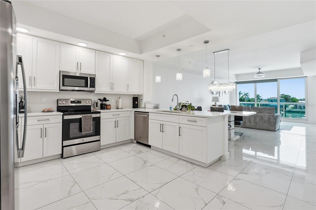 A modern white kitchen with stainless steel appliances, marble-look tile floors, and an island — 415 ISLAND WAY UNIT 204, CLEARWATER, FL