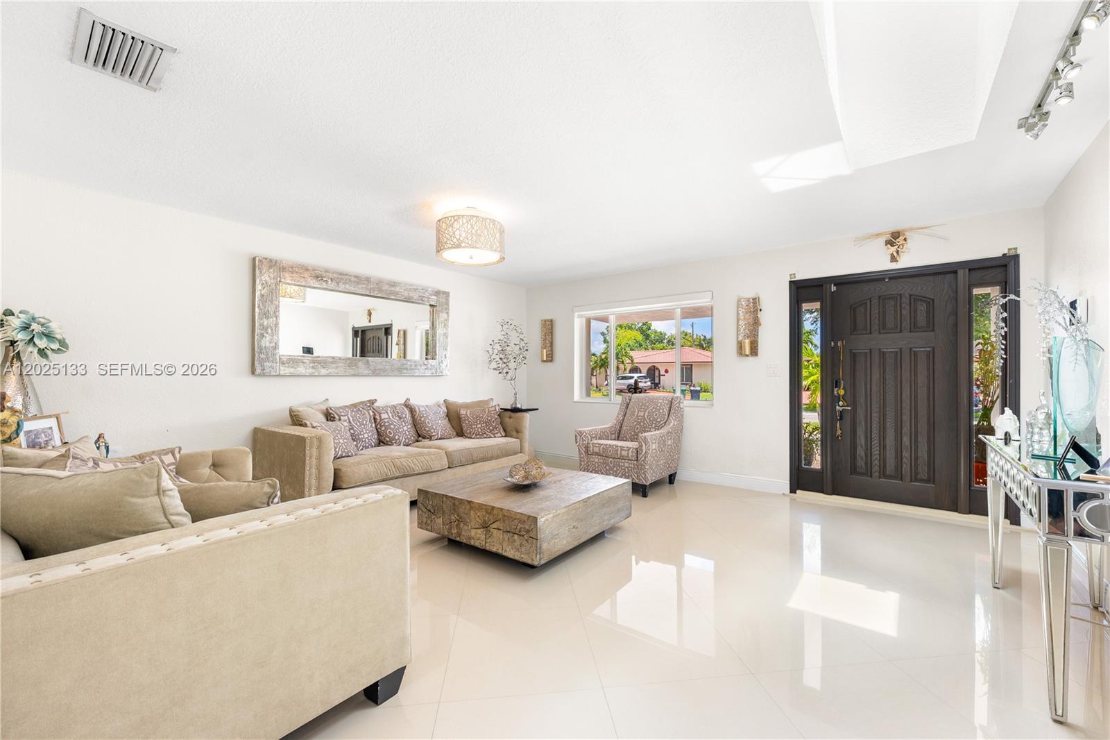 A bright living room features light tile floors, a large wooden coffee table, and a sofa — 16820 NW 74th Ave, Hialeah FL 33015, HIALEAH, FL