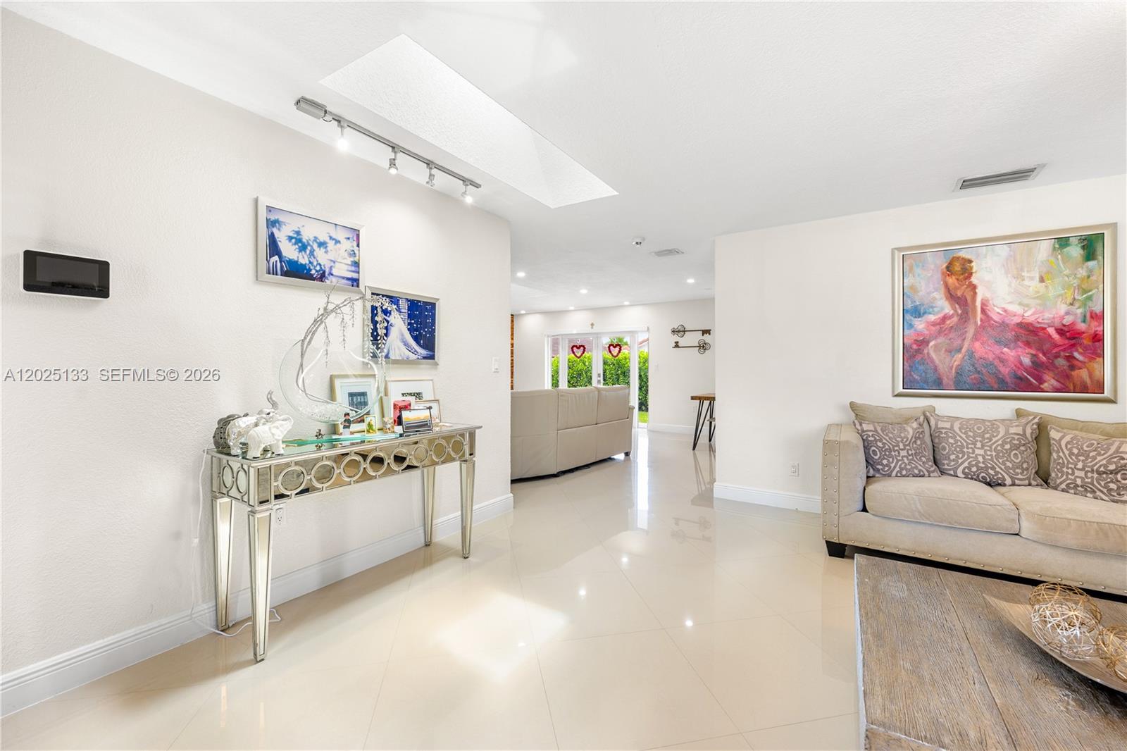 A bright living room features a mirrored console table, a beige sofa, and a skylight — 16820 NW 74th Ave, Hialeah FL 33015, HIALEAH, FL