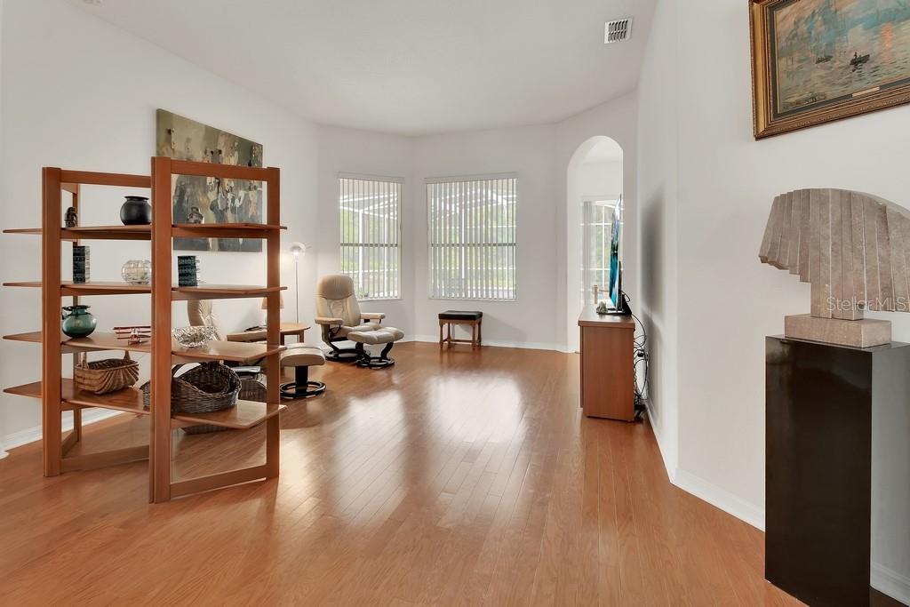 A bright living room features hardwood floors, a wooden shelving unit, and a recliner chair — 1483 W SILVER HAMMOCK, DELAND, FL