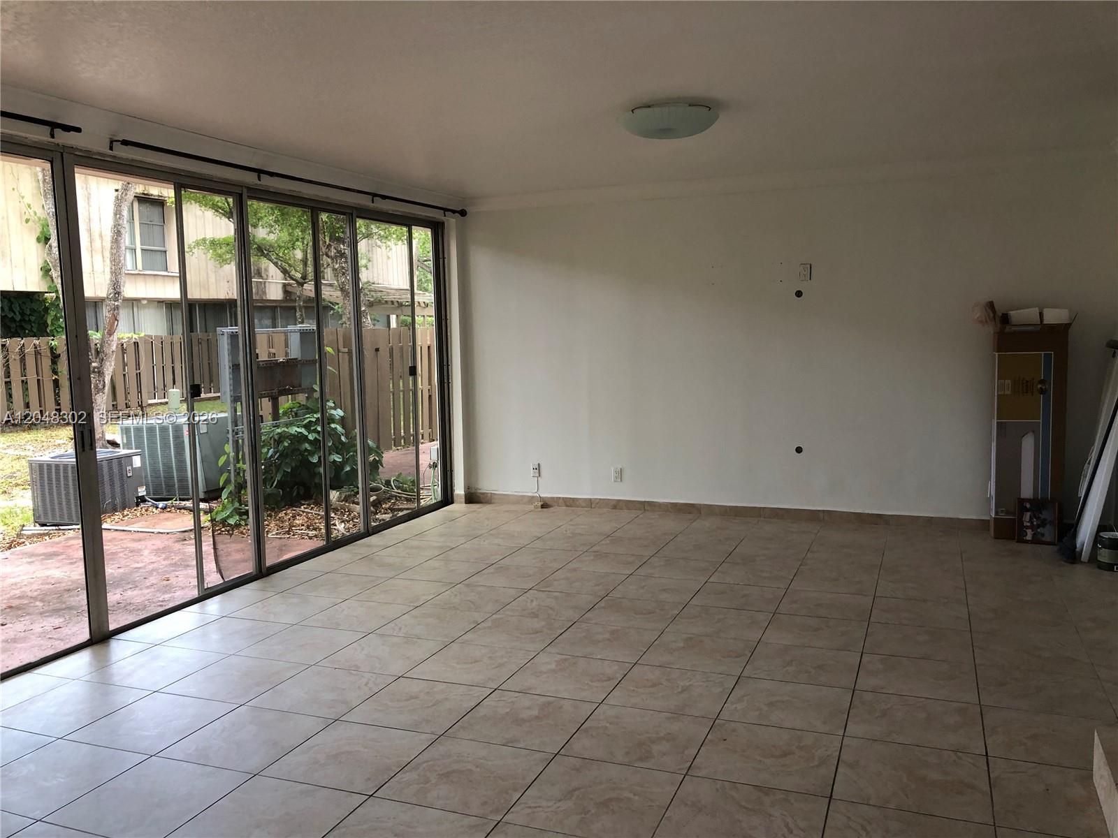 An empty room features large sliding glass doors, beige tile flooring, and white walls — 836 NW 82nd Ave # 3, Plantation FL 33324, PLANTATION, FL