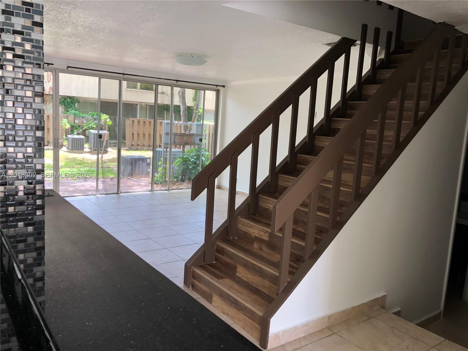 A staircase with brown railings and wood-look treads sits beside a room with sliding glass doors — 836 NW 82nd Ave # 3, Plantation FL 33324, PLANTATION, FL