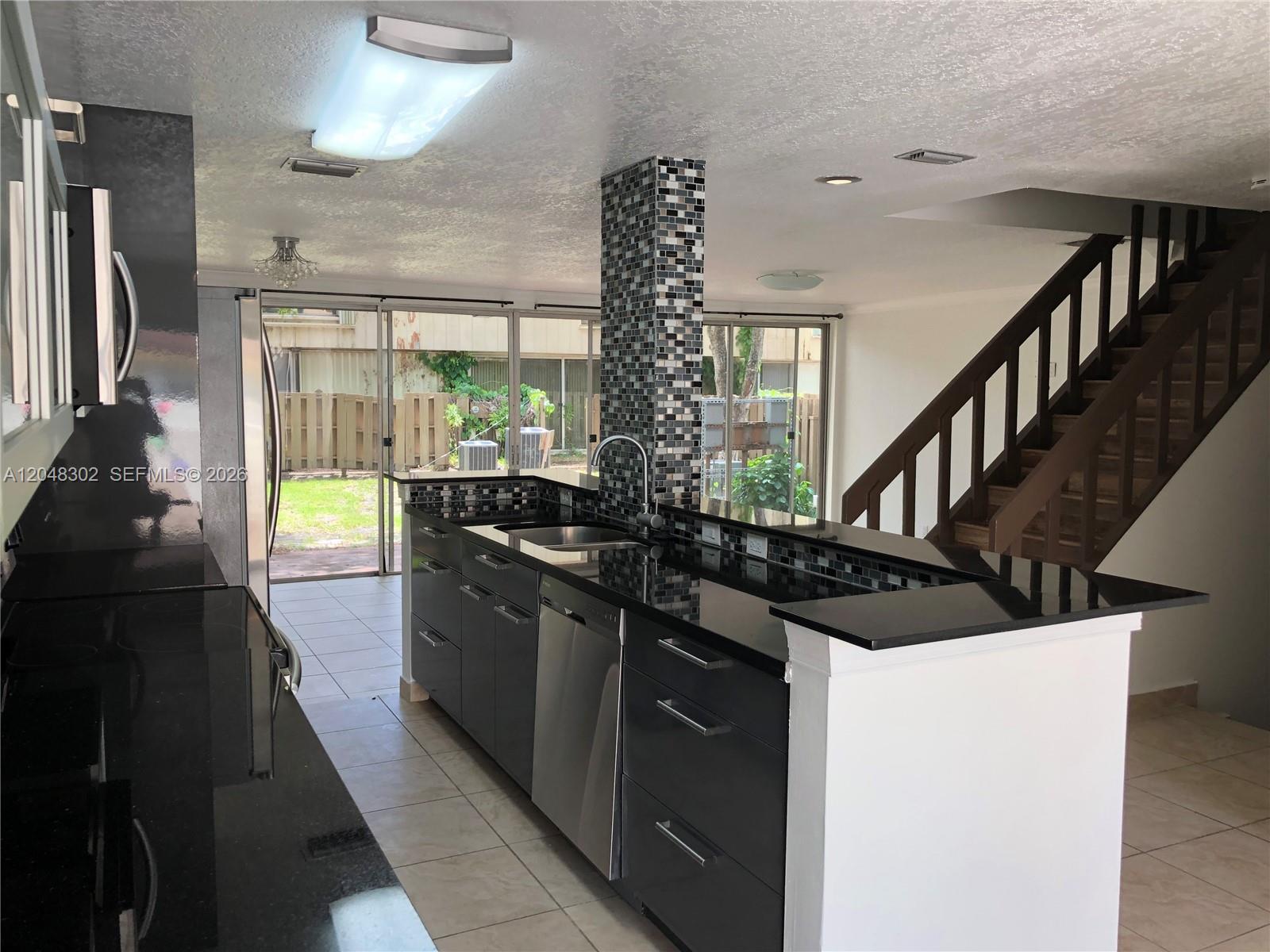 A kitchen features dark cabinetry, black countertops, a mosaic tile pillar, and an adjacent staircase — 836 NW 82nd Ave # 3, Plantation FL 33324, PLANTATION, FL