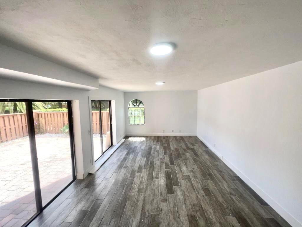 An empty room with wood-look tile flooring, white walls, and sliding glass doors to a patio — 8104 Severn Drive # B, Boca Raton FL 33433, BOCA RATON, FL