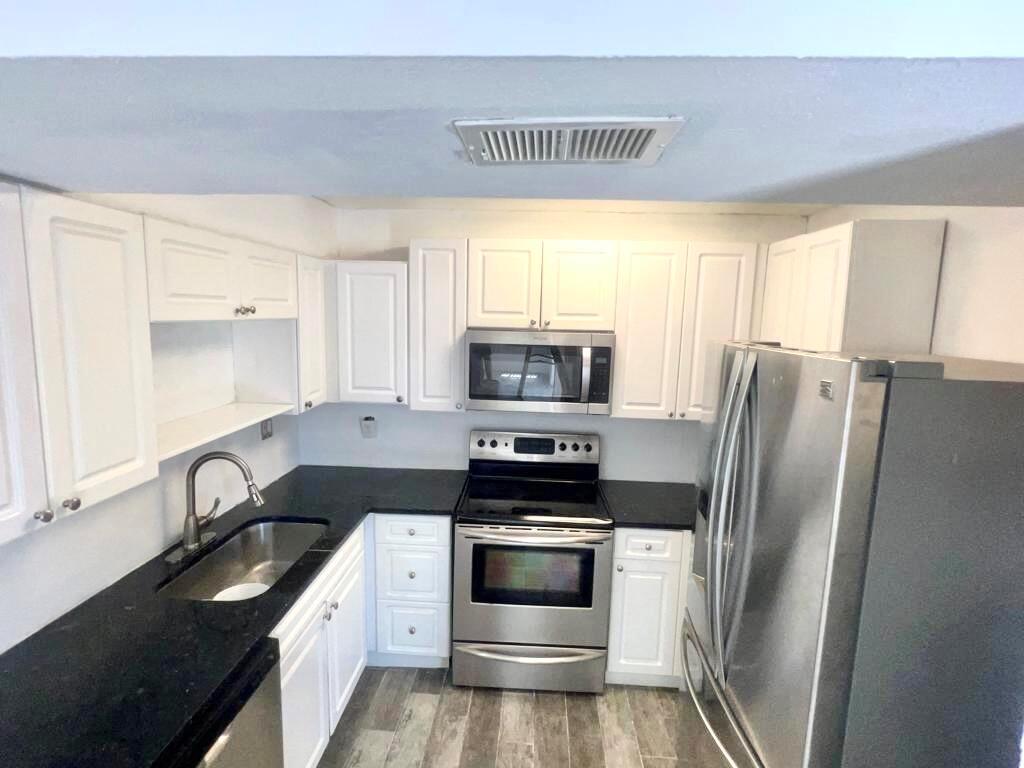 A kitchen features white cabinets, black countertops, stainless steel appliances, and wood-look flooring — 8104 Severn Drive # B, Boca Raton FL 33433, BOCA RATON, FL