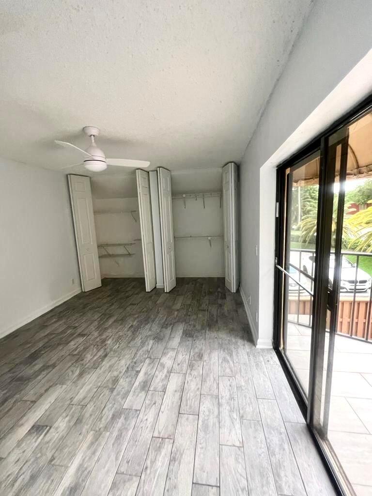 A bedroom with wood-look tile flooring, a ceiling fan, and open bi-fold closet doors — 8104 Severn Drive # B, Boca Raton FL 33433, BOCA RATON, FL