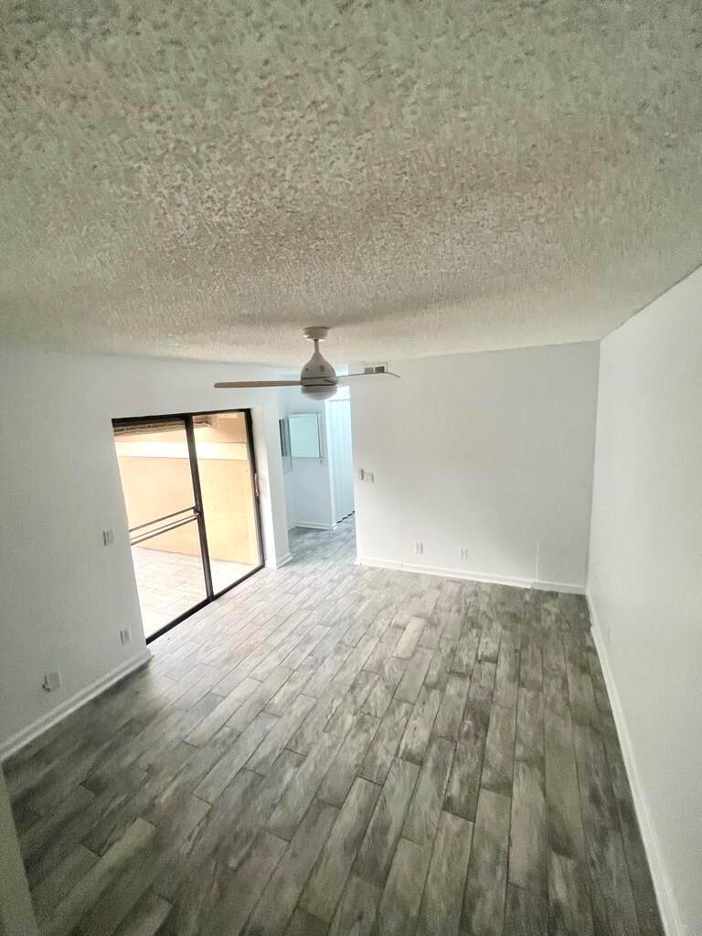 An empty room features gray wood-look flooring, a ceiling fan, and a sliding glass door — 8104 Severn Drive # B, Boca Raton FL 33433, BOCA RATON, FL