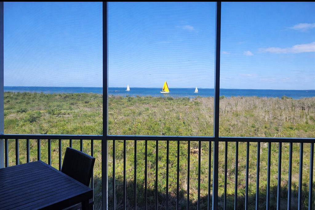 A view of the ocean and sailboats from a screened-in balcony with outdoor furniture — 3191 MATECUMBE KEY ROAD UNIT 307, PUNTA GORDA, FL