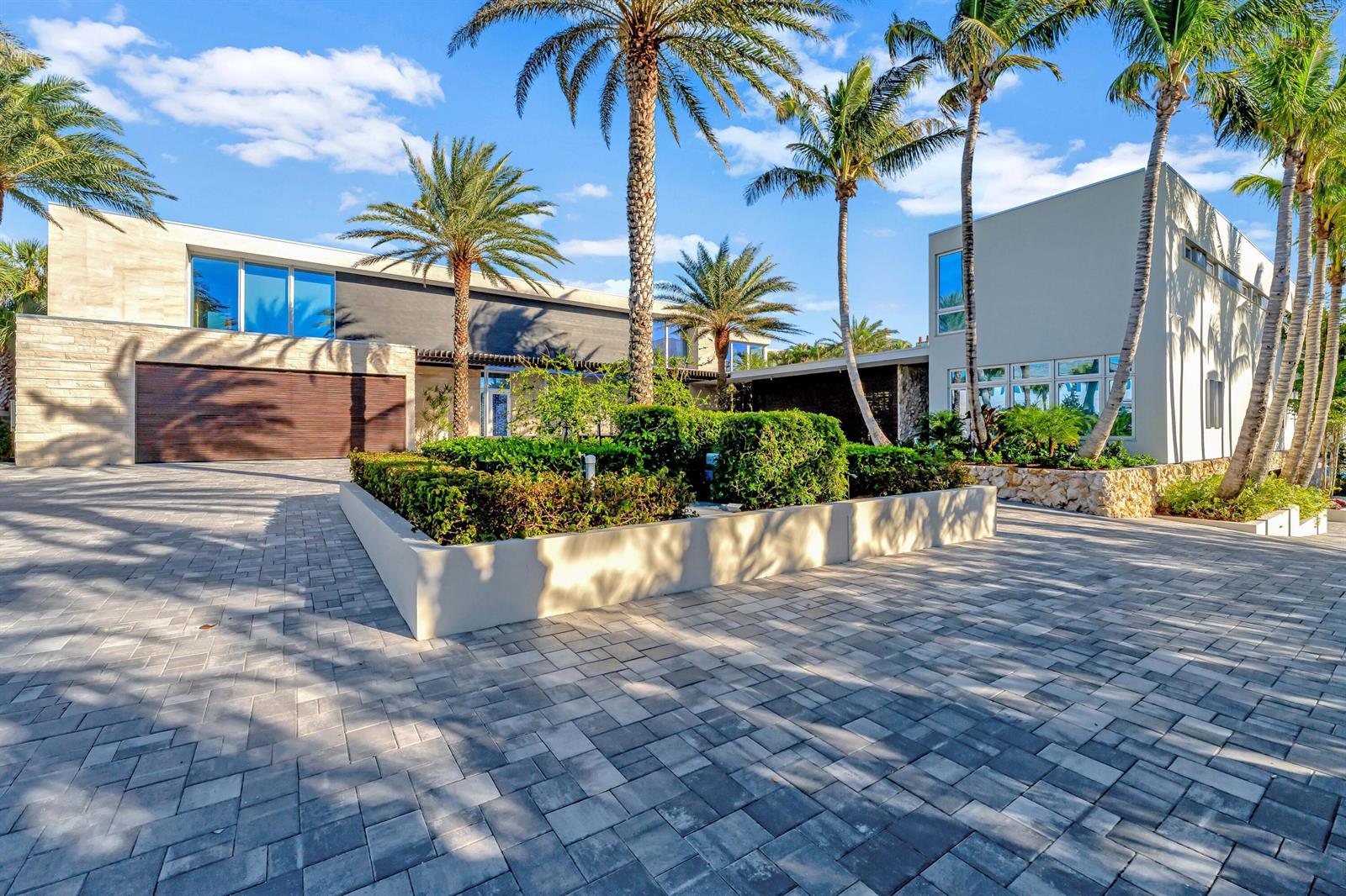 A modern house exterior with a paved driveway, palm trees, and a central garden planter — VERO BEACH, FL