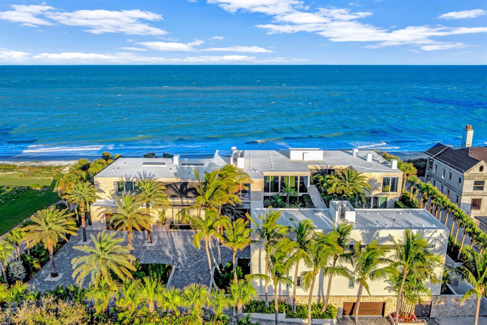 An aerial view of a modern beachfront mansion with palm trees and a paved courtyard — VERO BEACH, FL