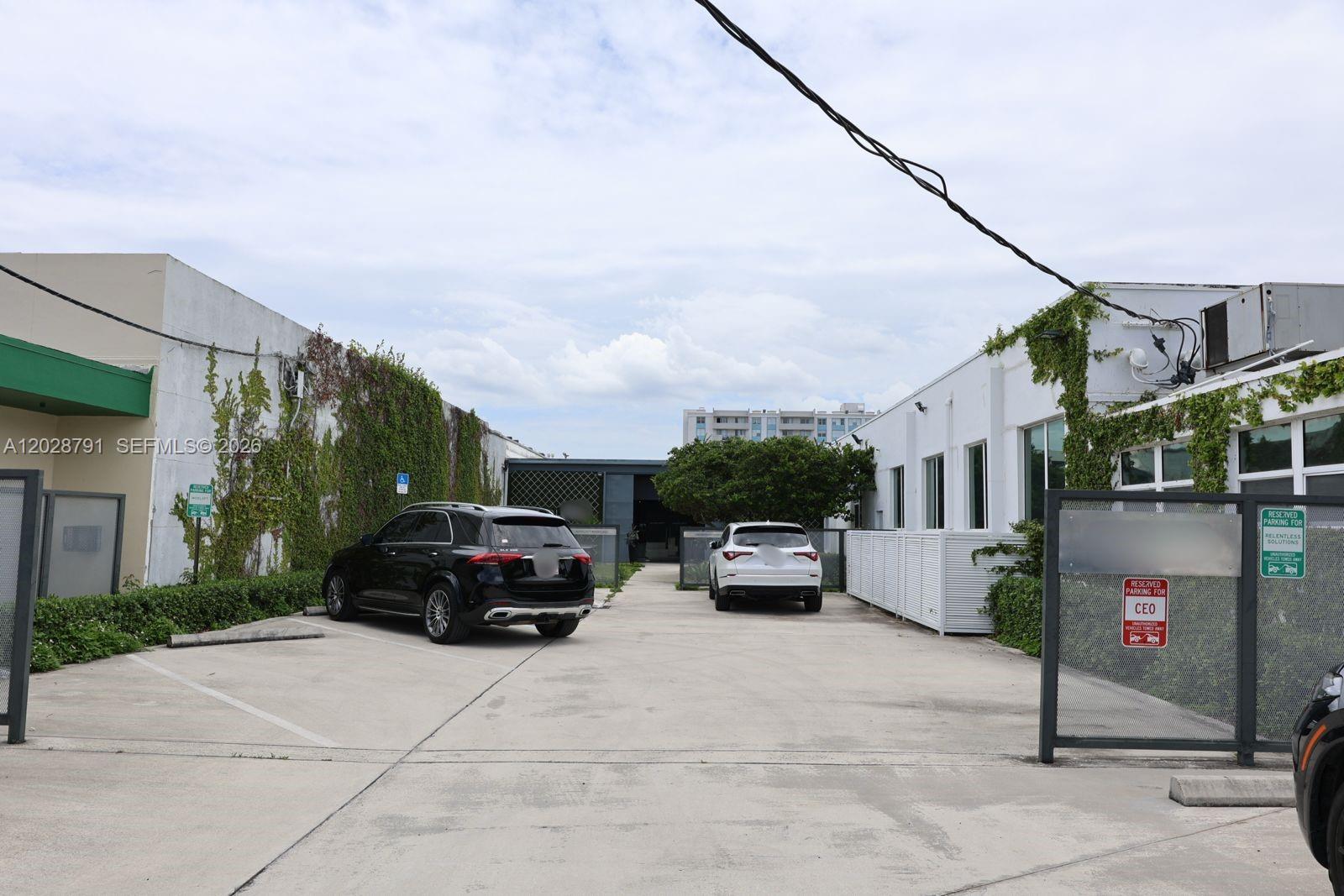 An outdoor parking area sits between two white buildings covered in climbing vines — 1810 NE 144th St, North Miami FL 33181, NORTH MIAMI, FL
