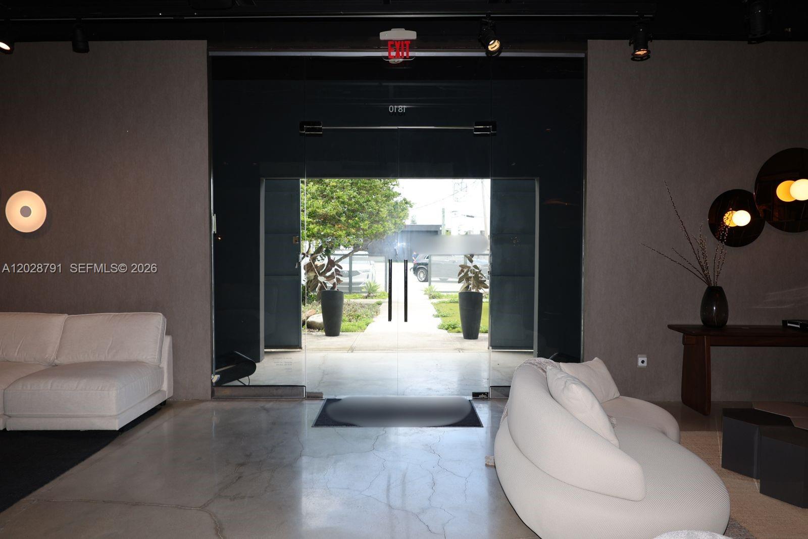 A modern interior space features a glass entrance, concrete floors, and white curved sofas — 1810 NE 144th St, North Miami FL 33181, NORTH MIAMI, FL