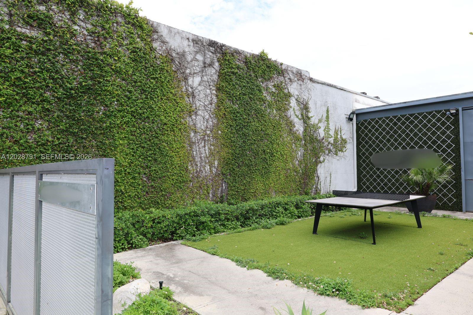 An outdoor area features a ping pong table on artificial turf beside a vine-covered wall — 1810 NE 144th St, North Miami FL 33181, NORTH MIAMI, FL