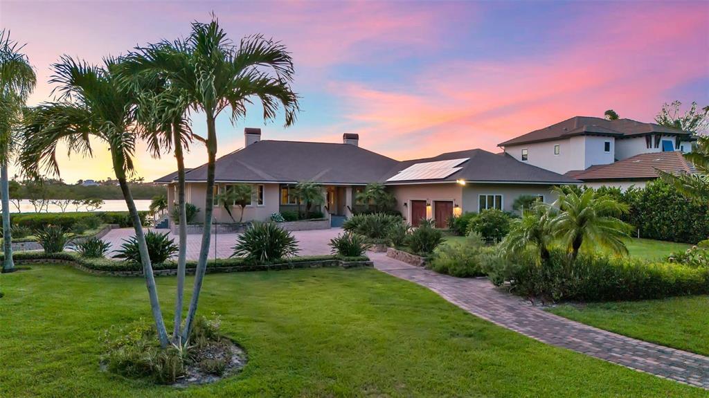 A single-story house with a paved driveway and palm trees at sunset near the water — 612 LAUREL ROAD W, NOKOMIS, FL