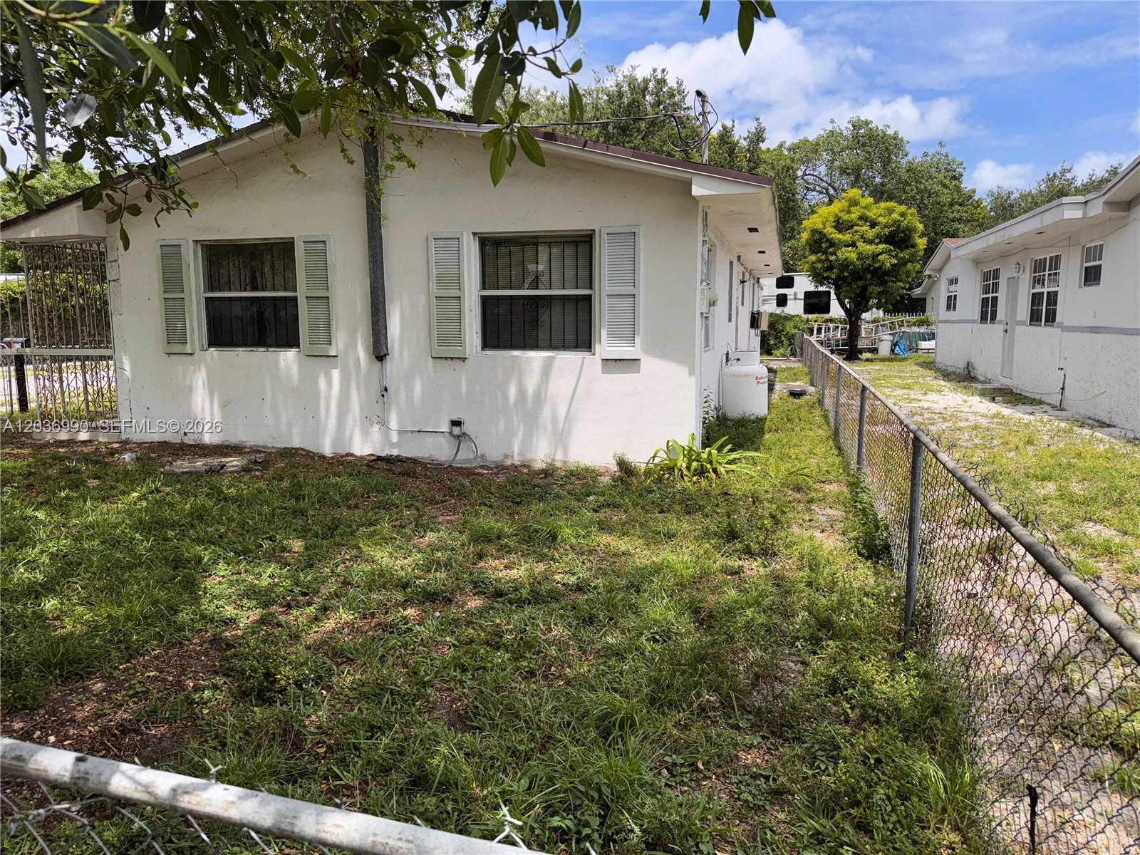A white house with green shutters sits behind a chain-link fence on a grassy lot — 7725 NW 14th Ave, Miami FL 33147, MIAMI, FL