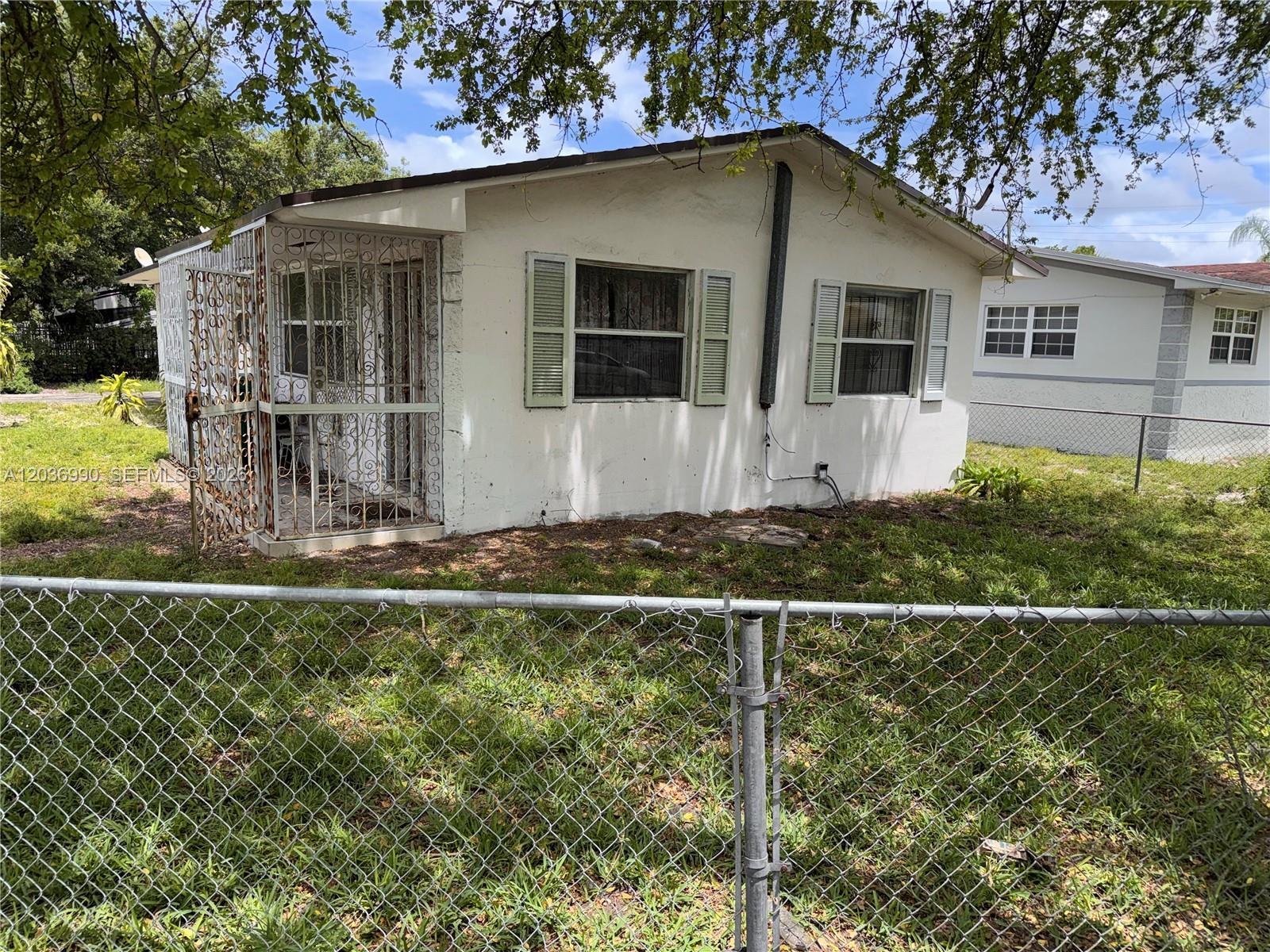 A small, white, single-story house with a metal security screen door and chain-link fencing — 7725 NW 14th Ave, Miami FL 33147, MIAMI, FL