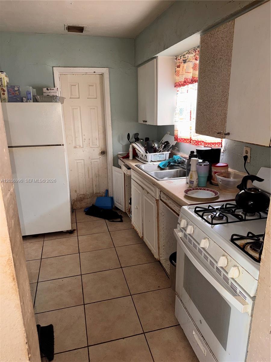 This kitchen features white appliances, tiled flooring, and wooden cabinets with a light blue wall — 7725 NW 14th Ave, Miami FL 33147, MIAMI, FL
