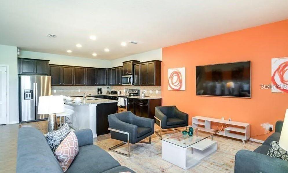 An open-concept kitchen and living room features dark cabinetry, stainless appliances, and an orange wall — 8817 CORCOVADO DRIVE, KISSIMMEE, FL