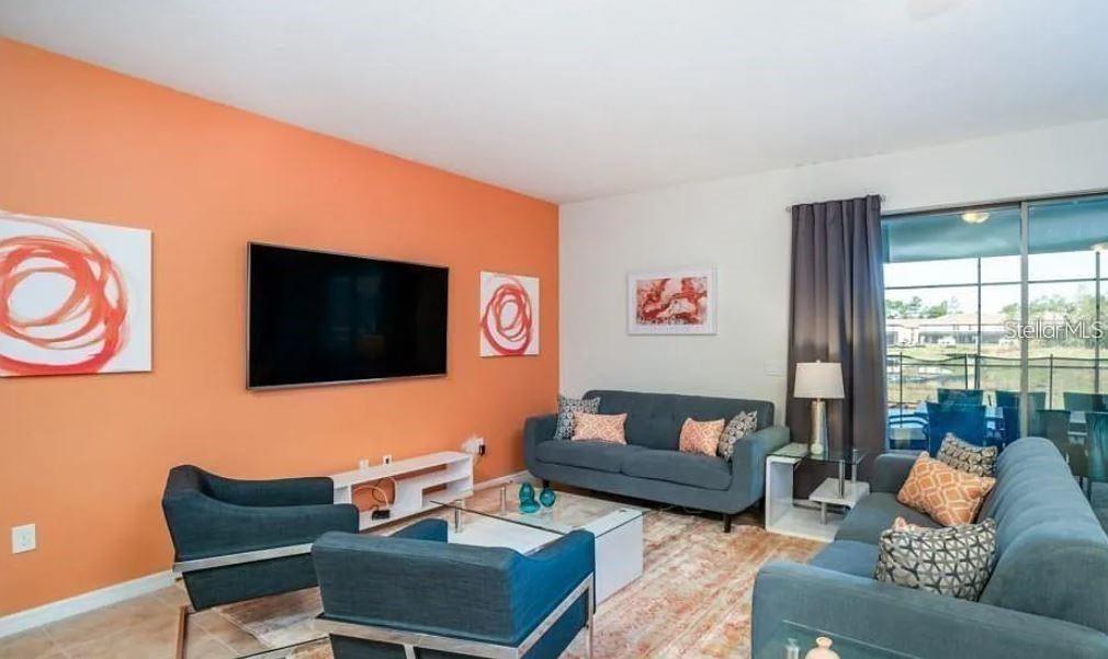 A living room features an orange accent wall, blue sofas, and a sliding glass door — 8817 CORCOVADO DRIVE, KISSIMMEE, FL